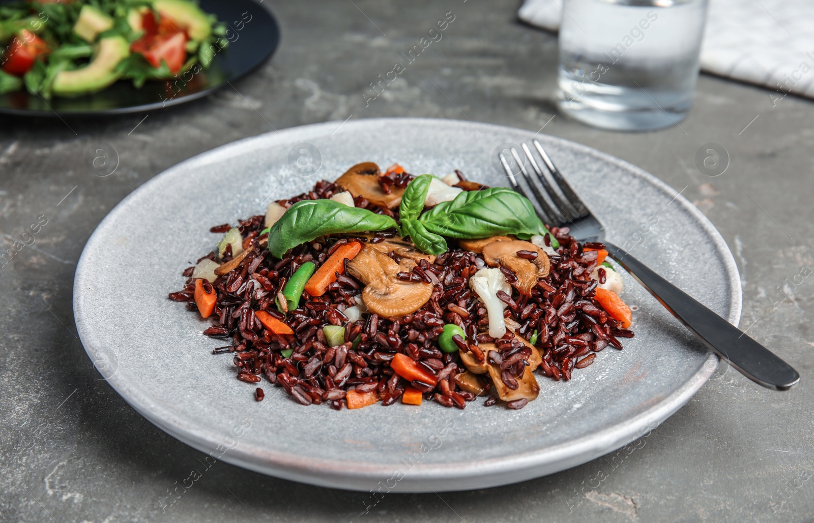 Photo of Plate of brown rice with vegetables on grey table