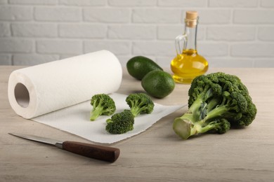 Photo of Paper towels, broccoli, avocados and knife on light wooden table