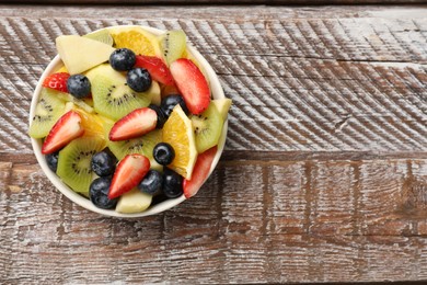 Photo of Tasty fruit salad in bowl on wooden table, top view. Space for text