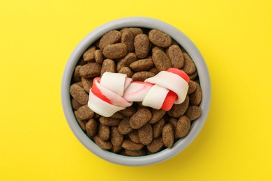 Chew bone and dry dog food on yellow background, top view