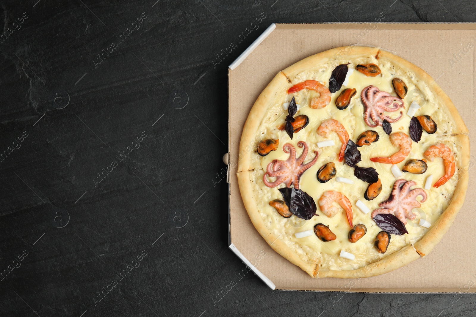 Photo of Delicious seafood pizza  in cardboard box on black table, top view. Space for text