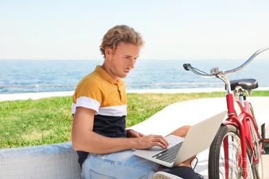 Photo of Attractive man with laptop and bike near sea