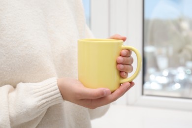 Photo of Woman holding yellow mug indoors, closeup. Mockup for design