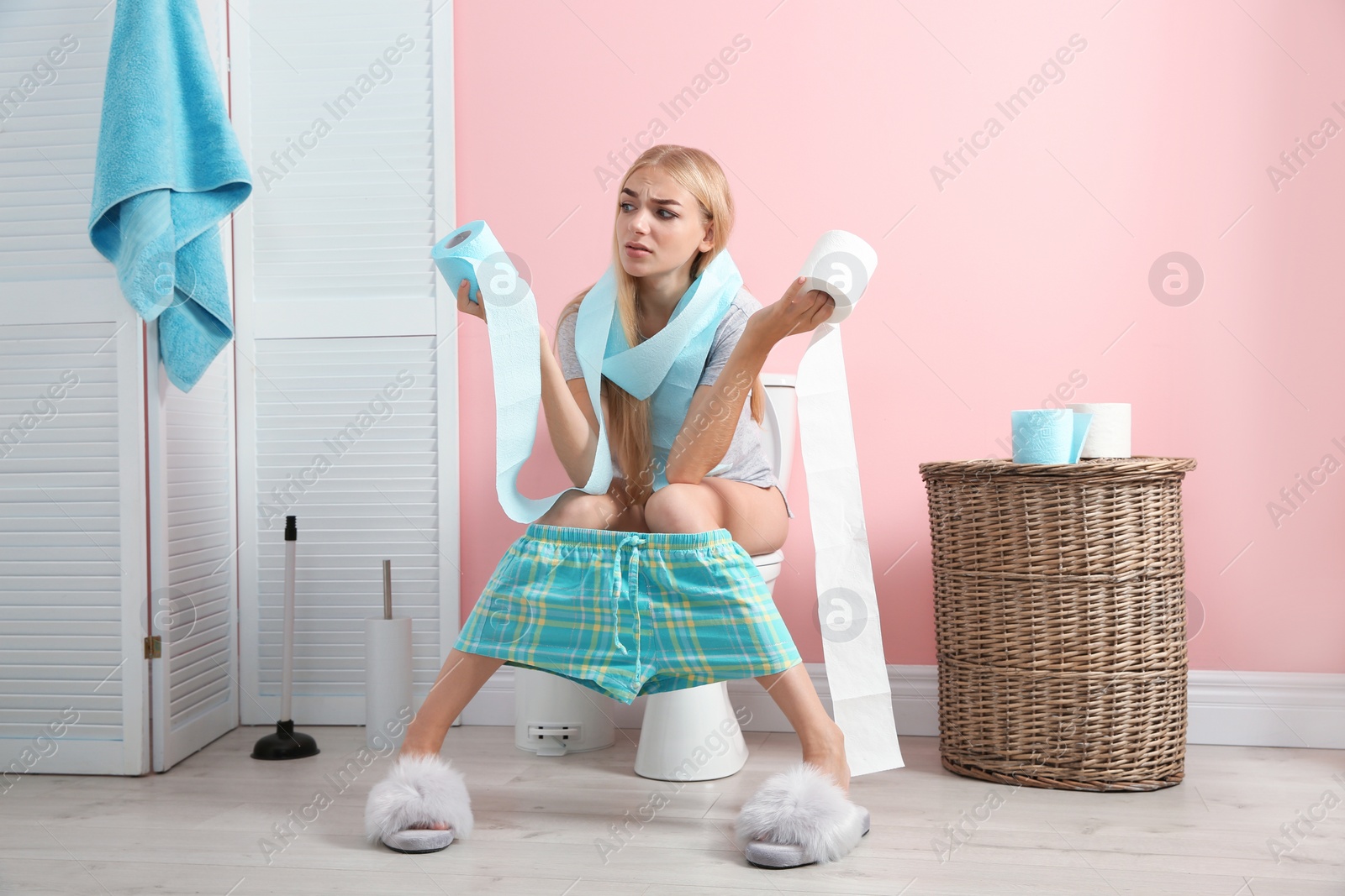 Photo of Woman with paper rolls sitting on toilet bowl in bathroom