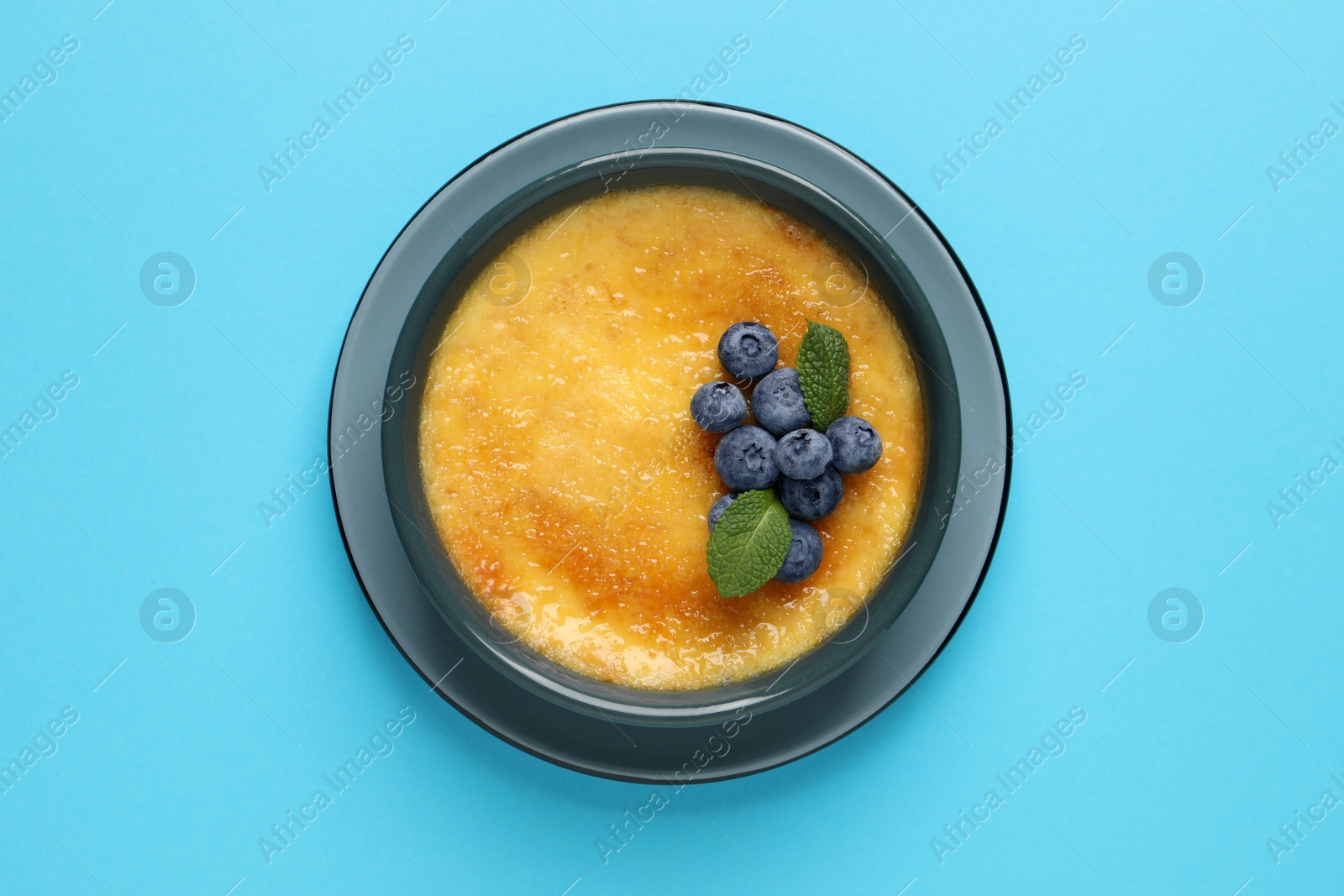 Photo of Delicious creme brulee with fresh blueberries and mint on light blue background, top view