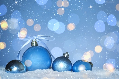 Beautiful light blue Christmas balls on snow against blurred festive lights, bokeh effect. Space for text