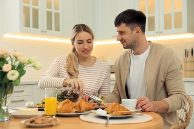 Photo of Happy couple having breakfast together at table in kitchen