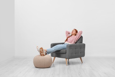 Beautiful young woman relaxing in armchair near white wall indoors