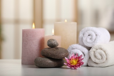 Photo of Spa composition. Burning candles, lotus flower, stones and towels on white table