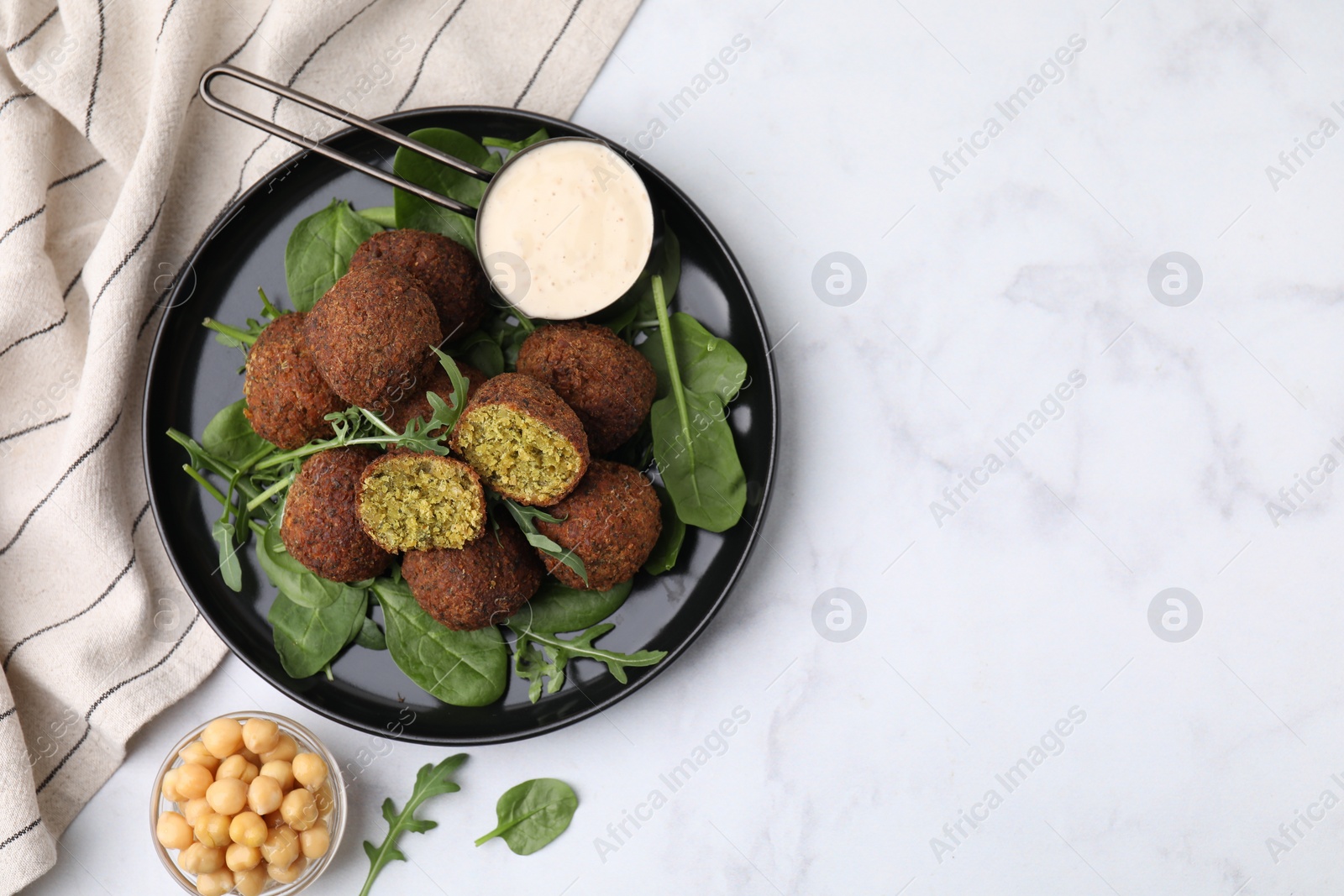 Photo of Delicious falafel balls, herbs, chickpeas and sauce on white marble table, top view. Space for text