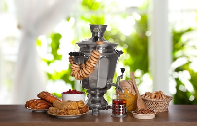 Image of Traditional Russian samovar and treats on wooden table against window in room