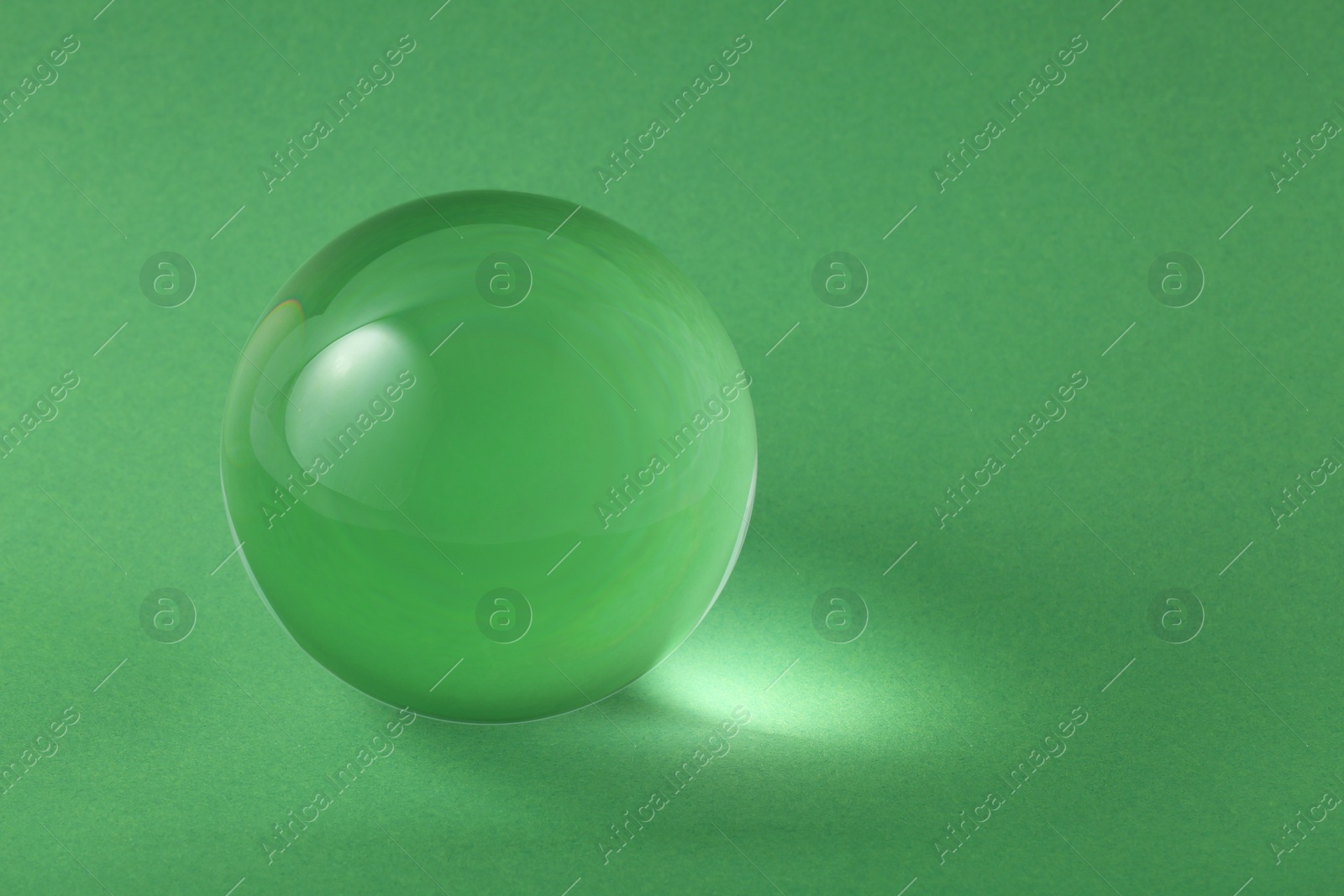 Photo of Transparent glass ball on light green background. Space for text