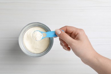 Photo of Woman taking powdered infant formula with scoop from can at white wooden table, top view