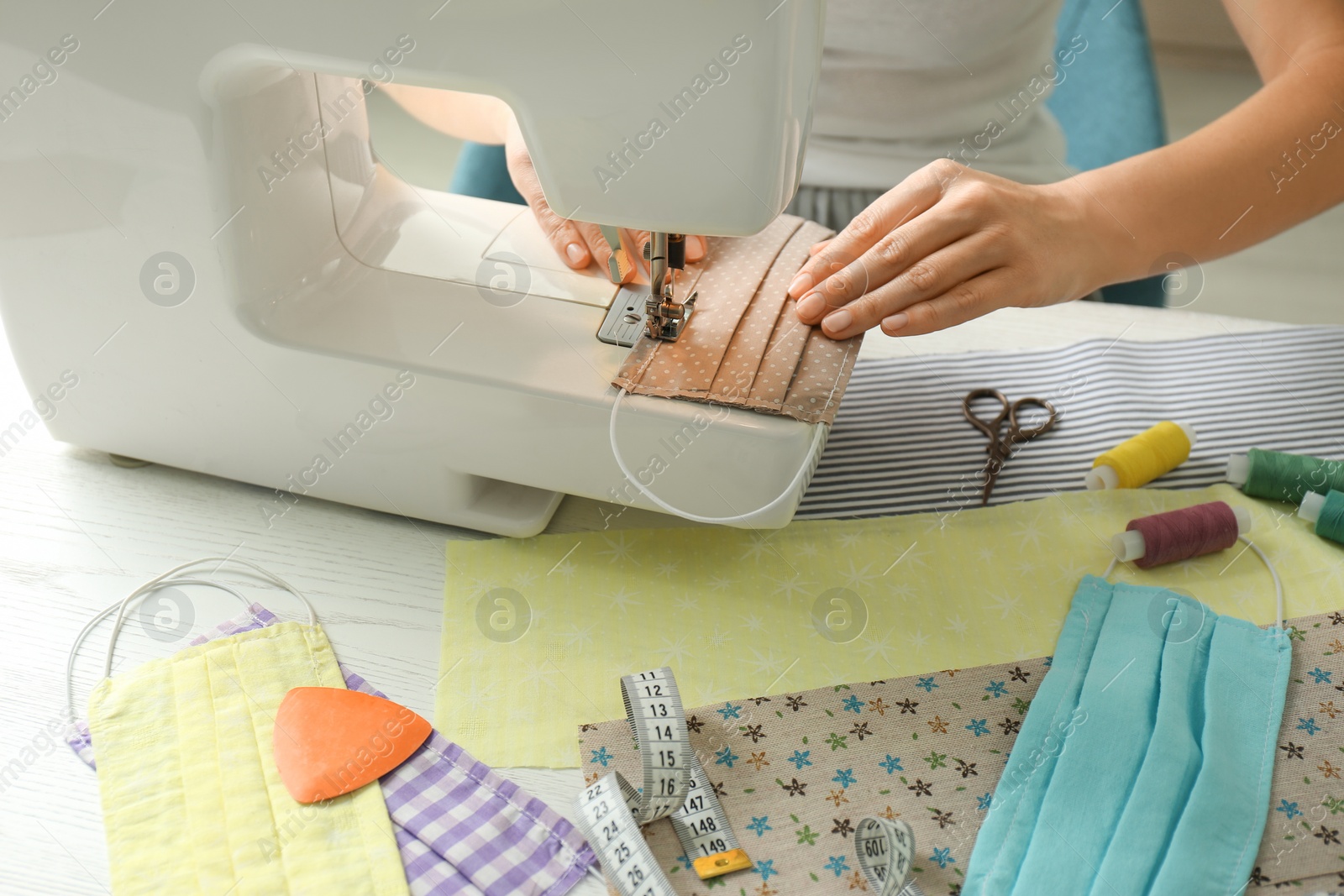 Photo of Woman sewing cloth mask with machine at table, closeup. Personal protective equipment during COVID-19 pandemic