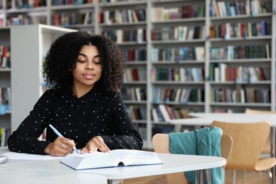 Photo of Young African-American woman studying at table in library