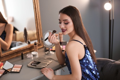 Portrait of beautiful woman applying makeup indoors