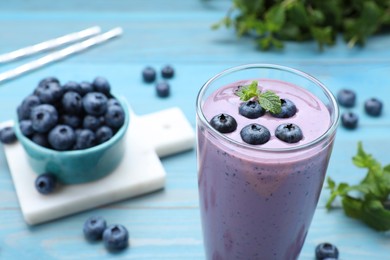 Photo of Glass of blueberry smoothie with mint and fresh berries on light blue wooden table. Space for text