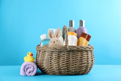 Photo of Wicker basket with different baby cosmetic products, toys and towel on light blue background