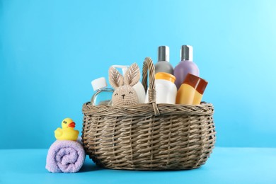 Wicker basket with different baby cosmetic products, toys and towel on light blue background