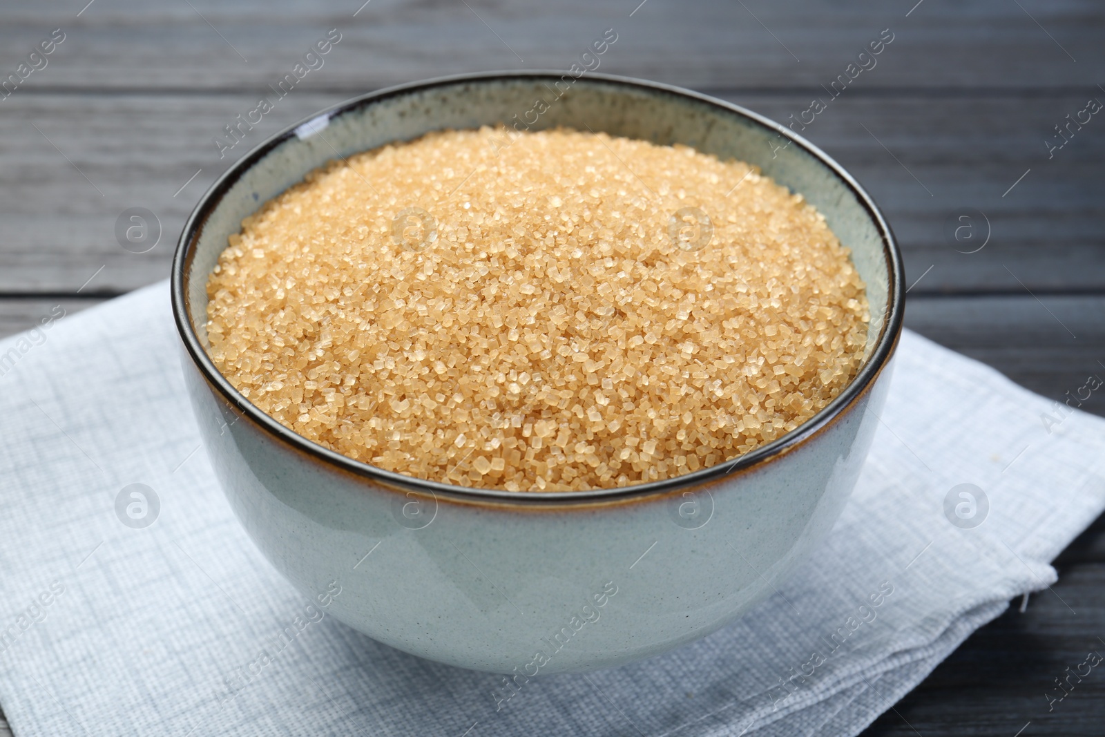 Photo of Brown sugar in bowl on black wooden table, closeup