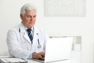 Senior doctor working with laptop at table in office