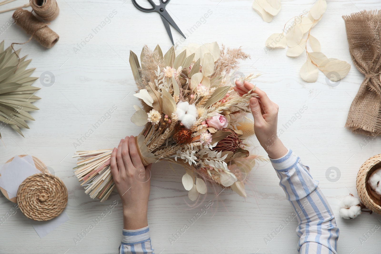 Photo of Florist making beautiful bouquet of dried flowers at white table, top view