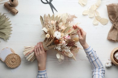 Photo of Florist making beautiful bouquet of dried flowers at white table, top view