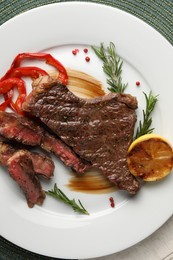 Photo of Delicious grilled beef steak with pepper, spices and lemon on table, top view
