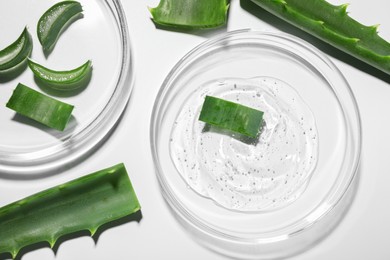 Photo of Petri dishes with cosmetic gel and cut aloe vera on white background, flat lay