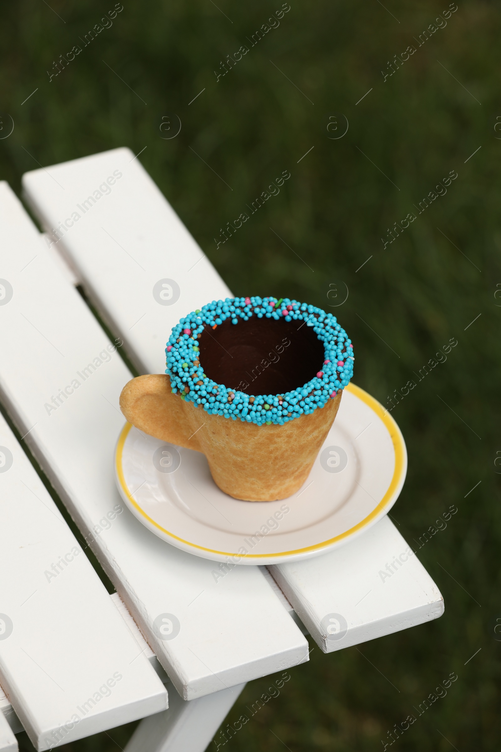 Photo of Delicious edible biscuit coffee cup decorated with sprinkles on white wooden table outdoors