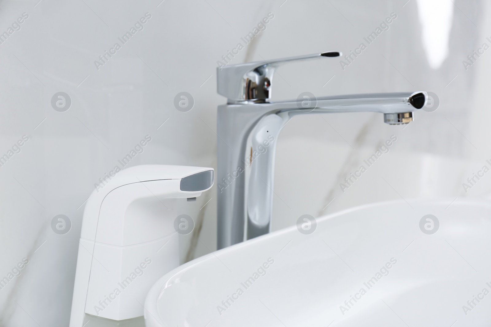 Photo of Modern automatic soap dispenser near sink in bathroom, closeup