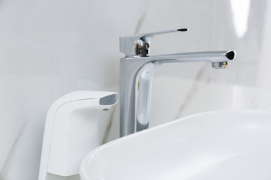 Modern automatic soap dispenser near sink in bathroom, closeup