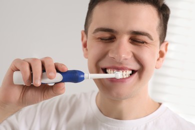 Photo of Man brushing his teeth with electric toothbrush indoors
