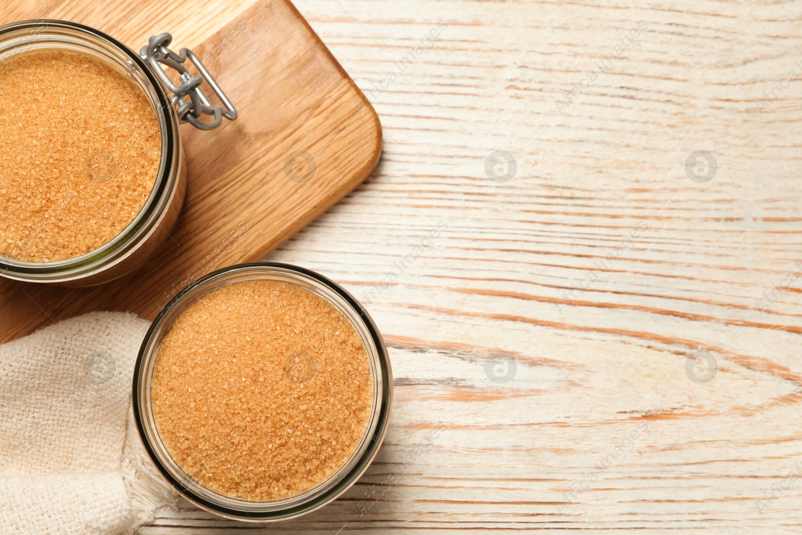 Photo of Glass jars with brown sugar on white wooden table, flat lay. Space for text