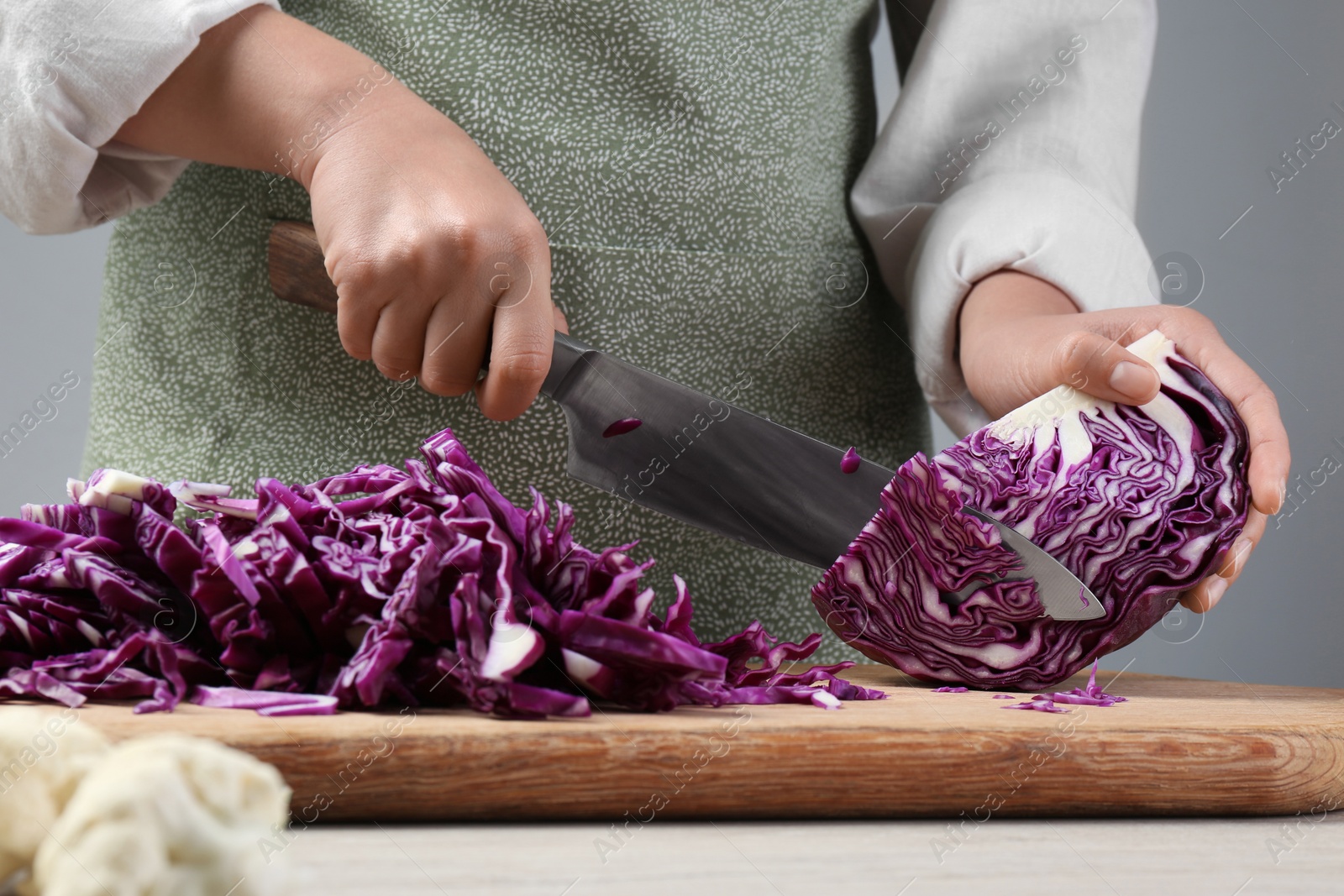 Photo of Woman cutting fresh radicchio cabbage on board at wooden table, closeup