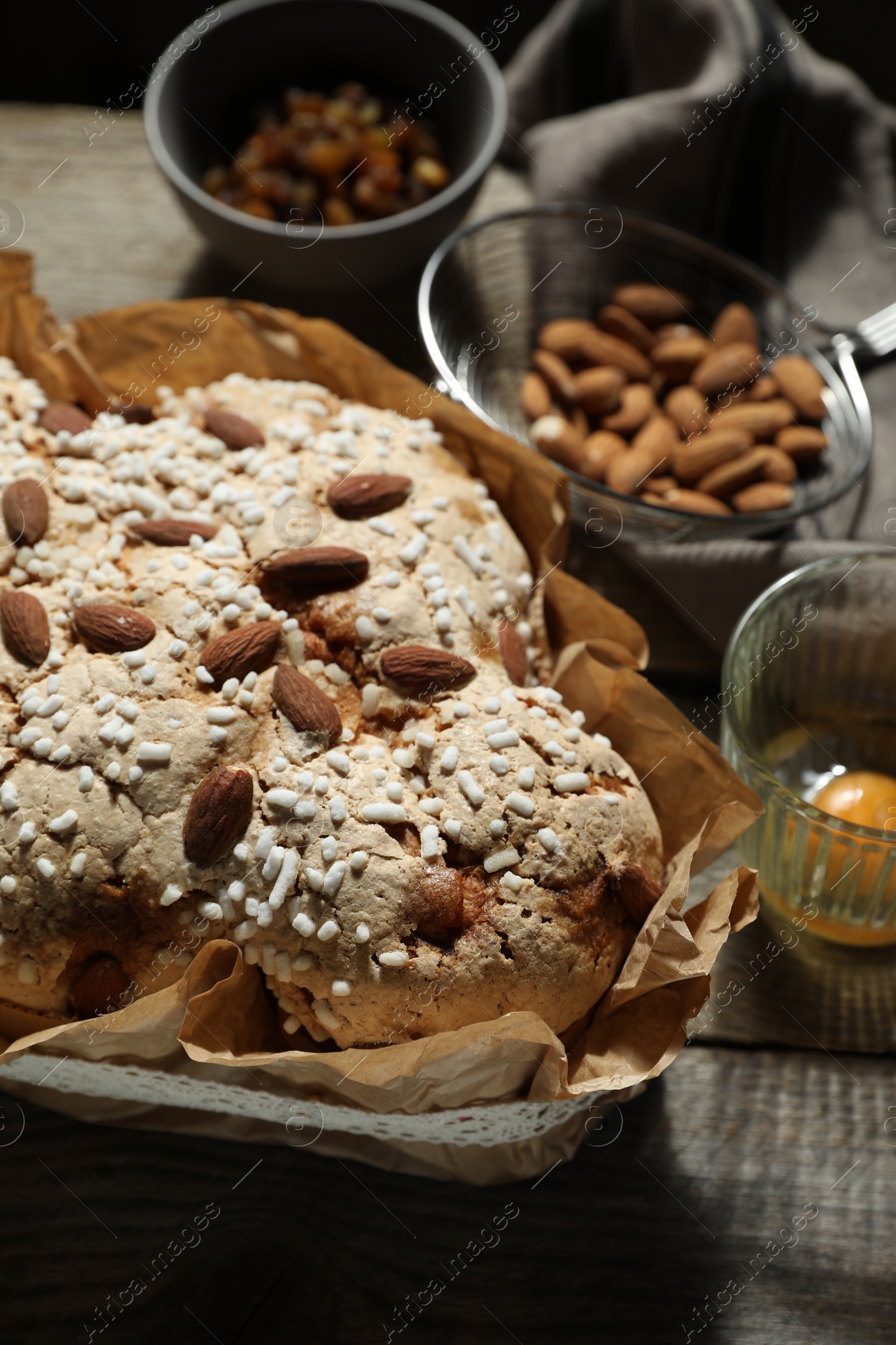 Photo of Delicious Italian Easter dove cake (traditional Colomba di Pasqua) and ingredients on wooden table, closeup