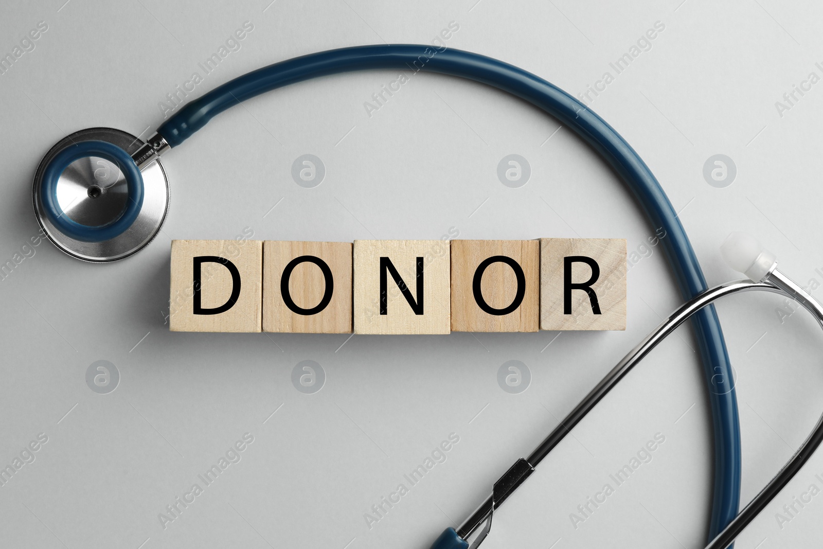 Photo of Word Donor made of wooden cubes and stethoscope on light grey table, flat lay