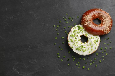 Photo of Delicious bagel with cream cheese and green onion on black table, flat lay. Space for text