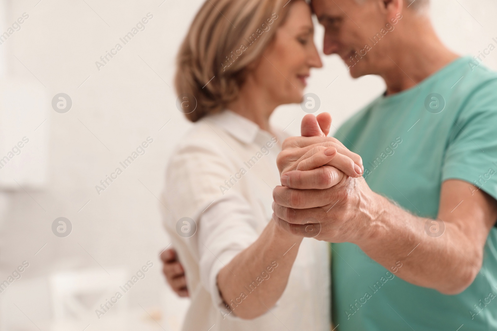 Photo of Happy senior couple dancing in kitchen, focus on hands