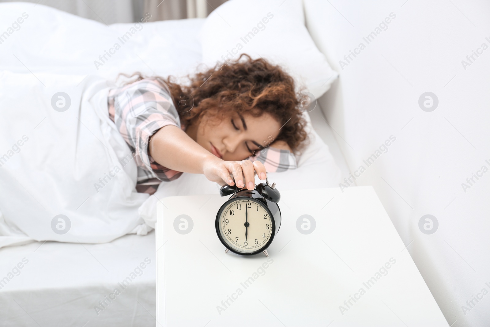 Photo of Young African-American woman turning off alarm clock at home. Bedtime