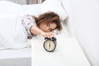 Young African-American woman turning off alarm clock at home. Bedtime