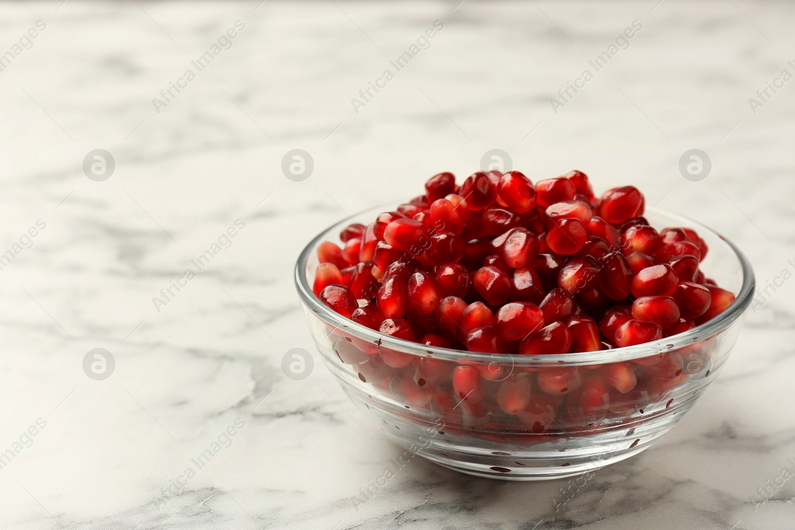 Photo of Ripe juicy pomegranate grains in bowl on white marble table, closeup. Space for text