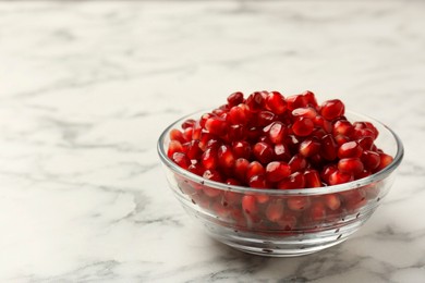 Ripe juicy pomegranate grains in bowl on white marble table, closeup. Space for text