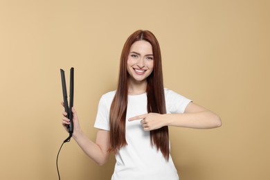 Photo of Beautiful woman pointing at hair iron on beige background