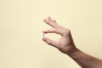 Photo of Man holding pill on beige background, closeup