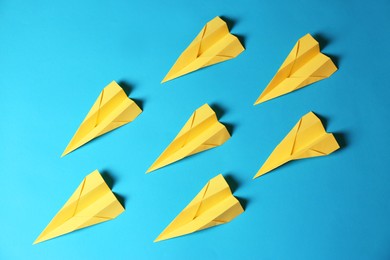 Photo of Many yellow paper planes on light blue background, flat lay