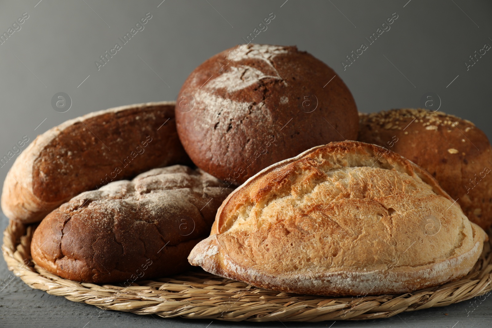 Photo of Wicker basket with different types of fresh bread on grey table, closeup