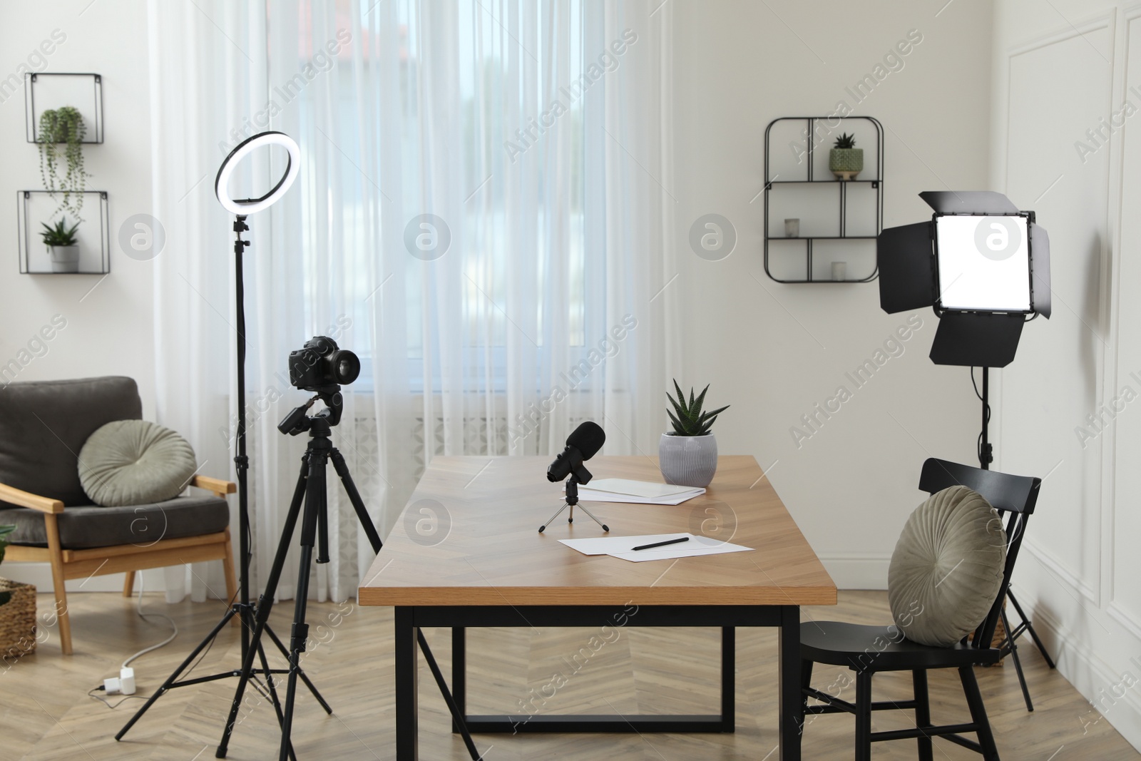 Photo of Camera and lighting equipment on tripods near table in room. Blogger workplace