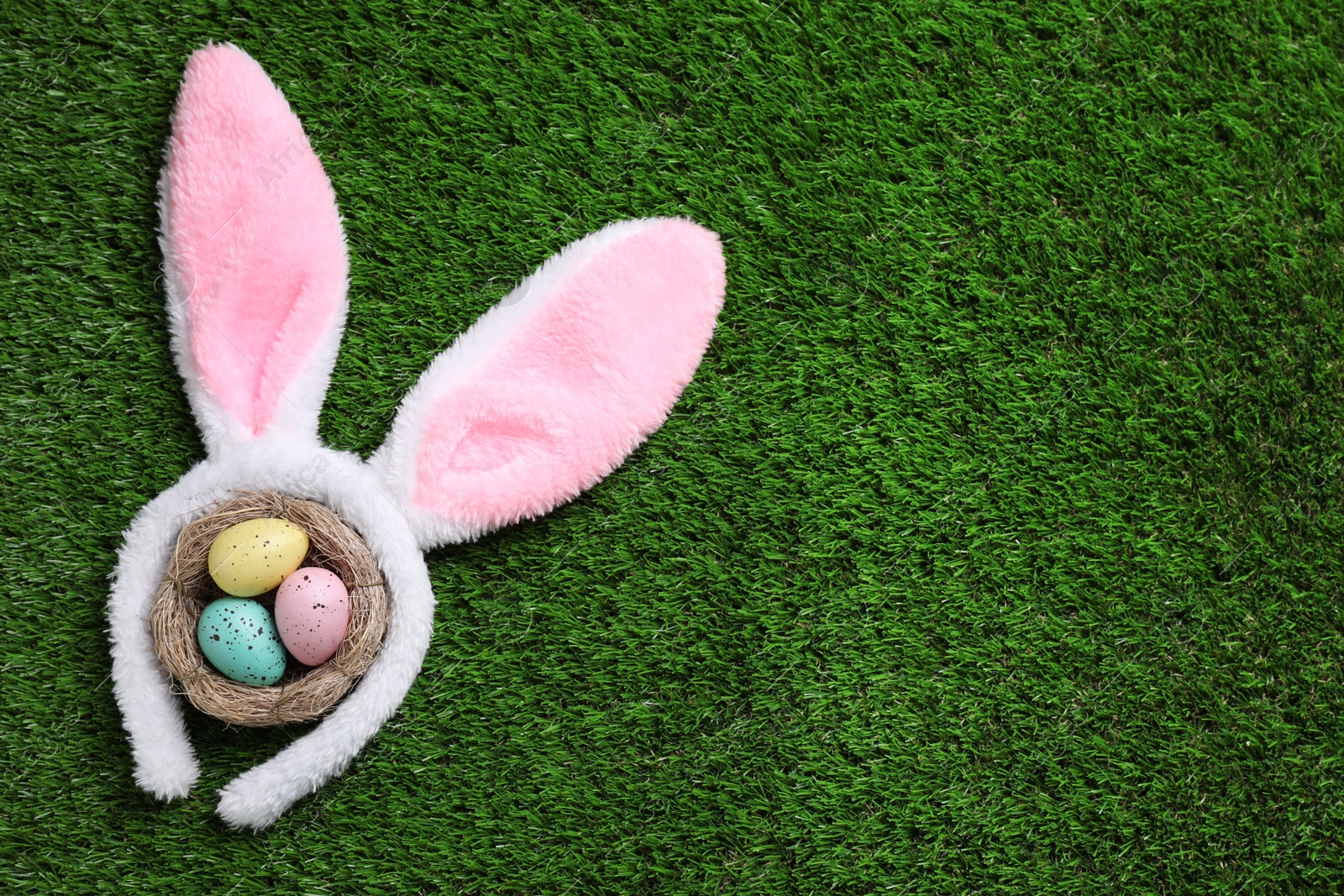 Photo of Headband with bunny ears, painted eggs and space for text on grass, flat lay. Easter holiday