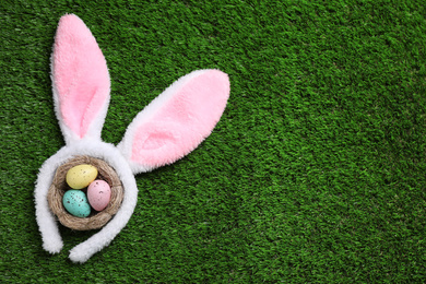 Photo of Headband with bunny ears, painted eggs and space for text on grass, flat lay. Easter holiday